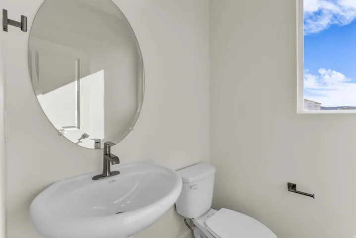 Pedestal sink with a single-handle faucet, oval wall mirror, and a fixed window