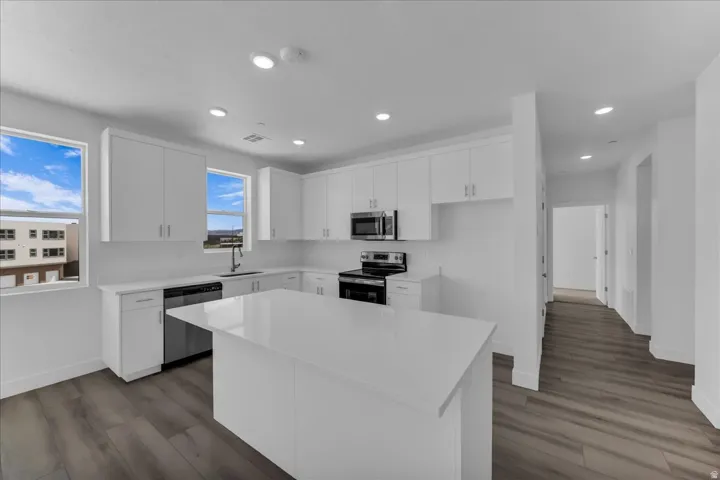 Modern kitchen featuring white cabinetry, a large center island, stainless steel appliances, recessed lighting, and wood-finish flooring