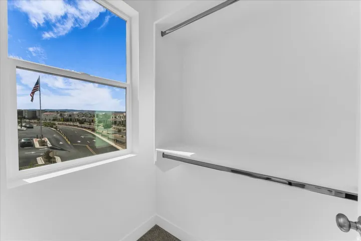 Window with white trim, built-in shelving, two hanging rods, and neutral carpeting
