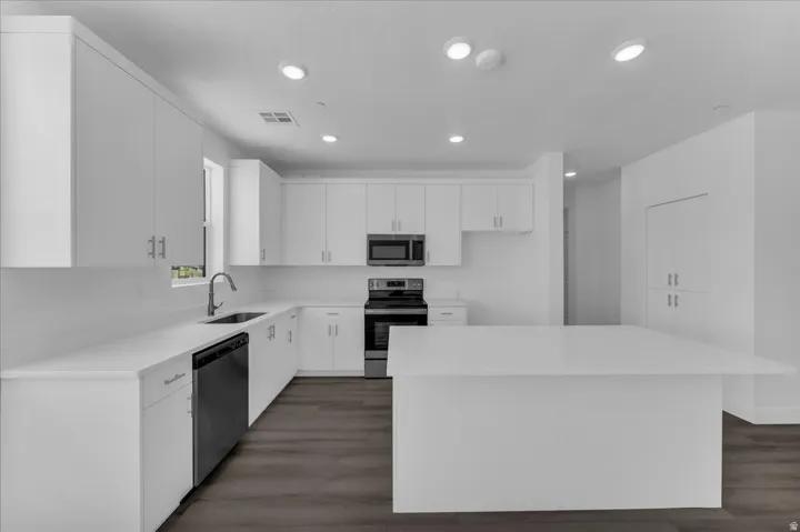 White cabinetry with brushed nickel hardware, stainless steel appliances, wood-finish flooring, recessed lighting, and a white countertop island