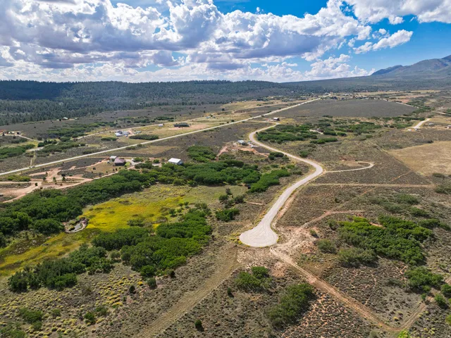 Expansive land with natural vegetation, winding paved road, distant mountain backdrop, scattered residential structures, and a small pond feature
