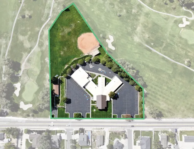 Expansive property featuring a multi-wing building, extensive asphalt parking, and a large grass field with a baseball diamond