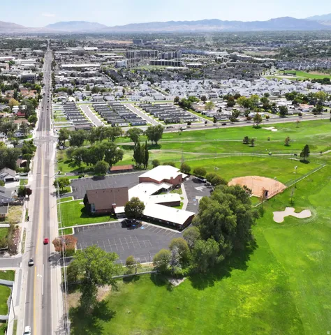 Expansive property featuring a multi-building complex, a large paved parking area, and surrounding green spaces with mature trees