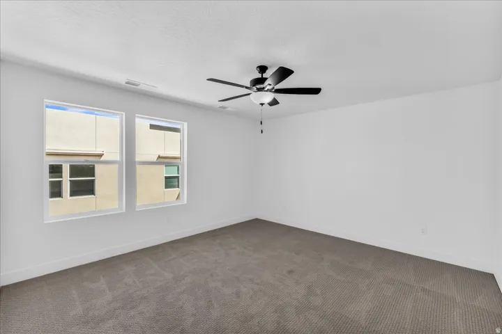 Two large windows, ceiling-mounted light fixture with fan, and wall-to-wall carpeting