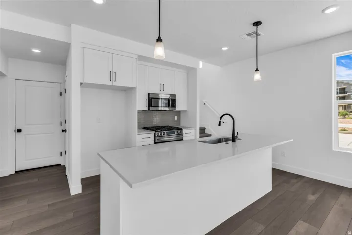 White cabinetry, stainless steel appliances, dark wood-finish flooring, recessed lighting, and a kitchen island with a built-in sink and matte black faucet