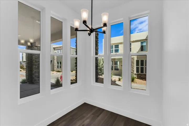 White walls with wood-finish flooring, featuring a contemporary chandelier and multiple vertical windows