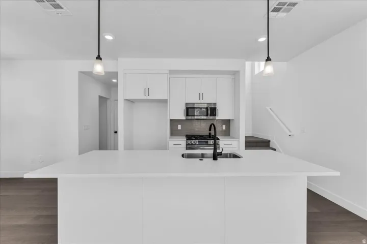 Kitchen island with integrated sink and matte black faucet, white cabinetry, built-in microwave, and wood-finish flooring