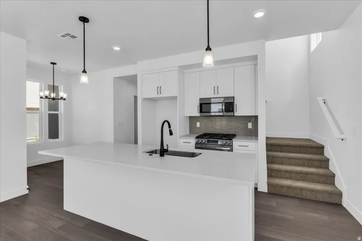 Modern kitchen featuring a large island, stainless steel appliances, white cabinetry, and wood-finish flooring