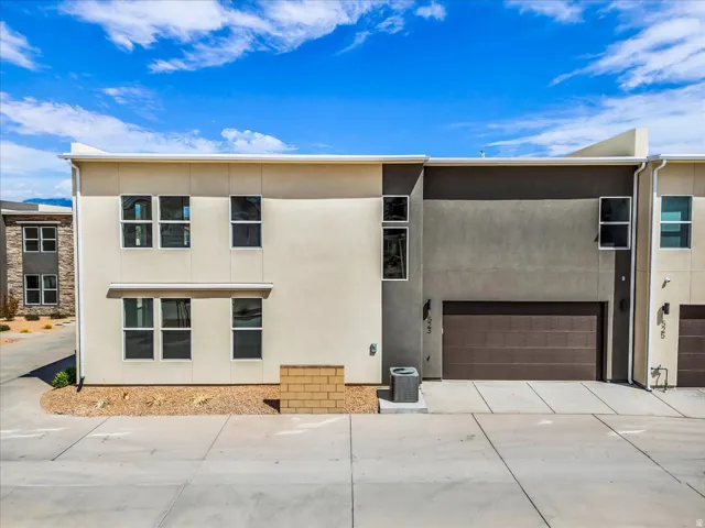 Contemporary townhome exterior featuring multi-toned stucco, multiple windows, an attached garage, and a concrete driveway