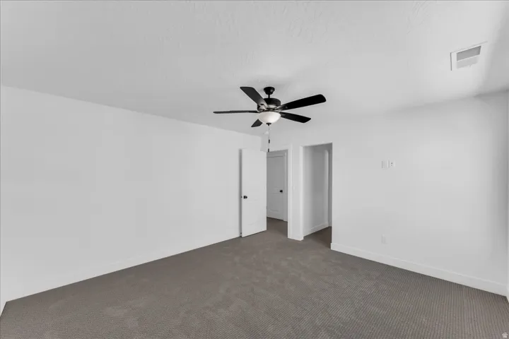Spacious interior featuring neutral carpeting, white walls, and a ceiling fan with integrated lighting