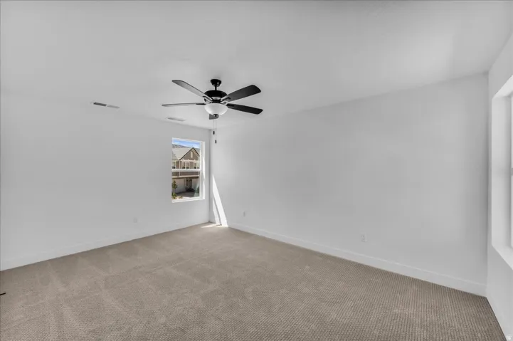 Spacious room featuring neutral carpeting, a ceiling fan with integrated lighting, and white walls