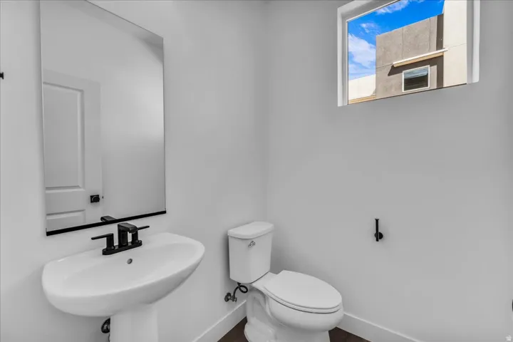 Pedestal sink with a matte black faucet, wall-mounted mirror, and a fixed window
