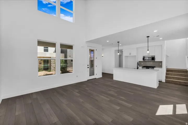 Wood-finish flooring, high ceilings, upper-story windows, white cabinetry, and modern pendant lighting