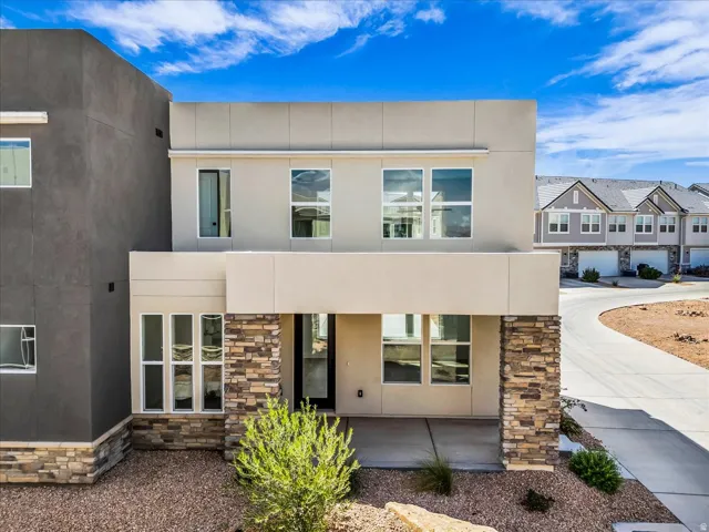 Contemporary exterior featuring a stone accent facade, stucco finish, multiple windows, a covered entry, and a concrete driveway