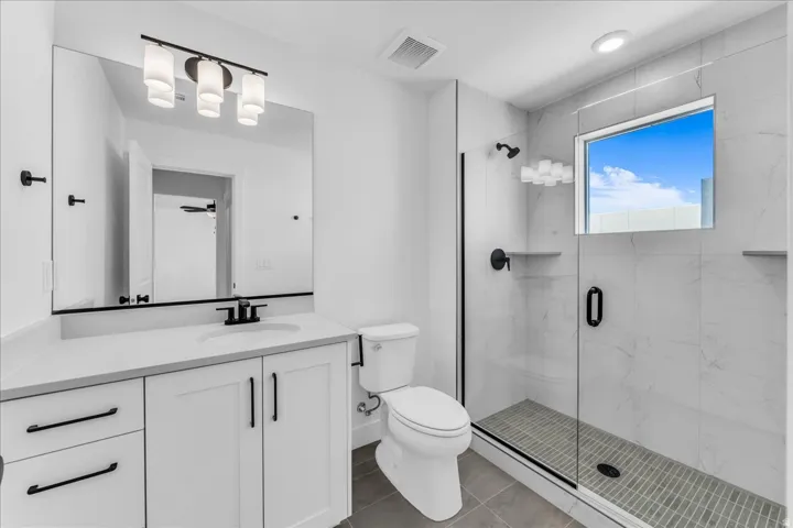 White shaker-style vanity with a single basin sink, matte black hardware, and an expansive mirror