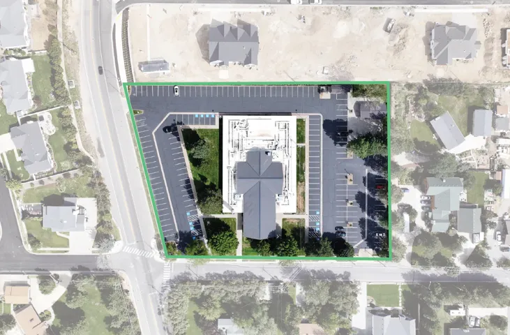 Expansive asphalt parking area, mature landscaping, multi-level building with a gabled roof, and a surrounding green border