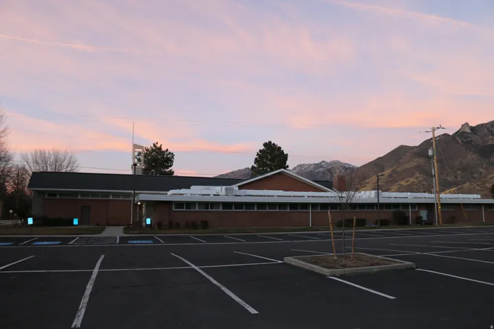 Brick exterior with multiple windows, prominent mountain scenery, and a large paved parking area
