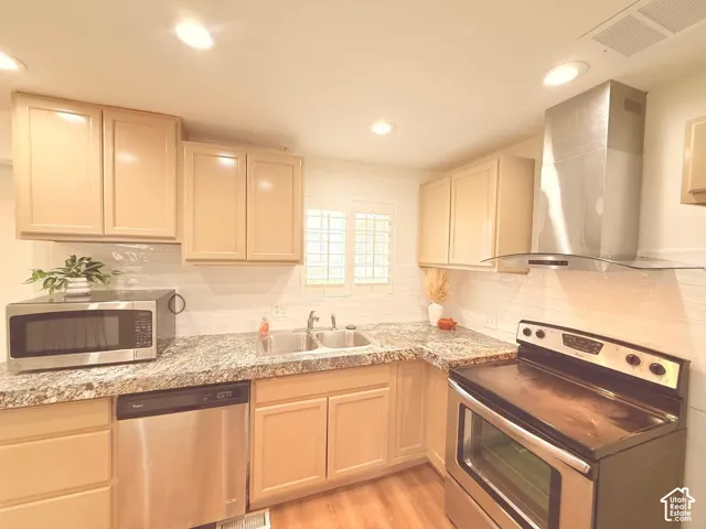 Kitchen featuring wood-finish flooring, light-toned cabinetry, stainless steel appliances, a double basin sink, and a tiled backsplash