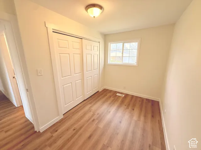 Wood-finish flooring, white paneled closet doors, single window with white trim, and a flush-mount ceiling light fixture