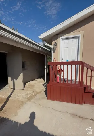 Stucco exterior with white trim, wood-toned porch with railing, white panel door, and exterior wall sconce
