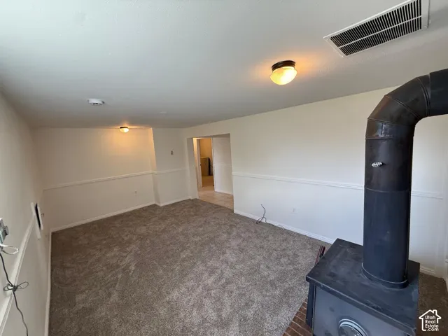 Carpeted room with wainscoting, a wood-burning stove, and overhead lighting