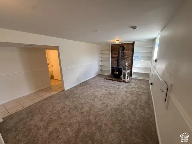 Carpeted flooring, brick accent wall with a wood-burning stove, built-in shelving, and tile flooring