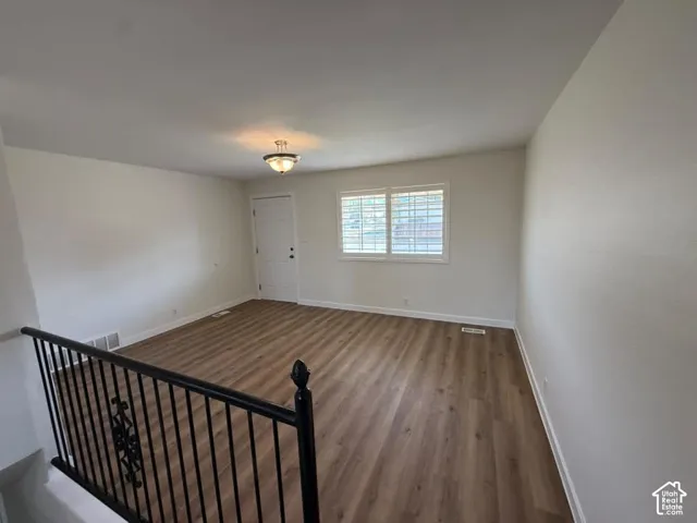 Wood-finish flooring, neutral wall tones, window with white blinds, white entry door, and a decorative ceiling light fixture