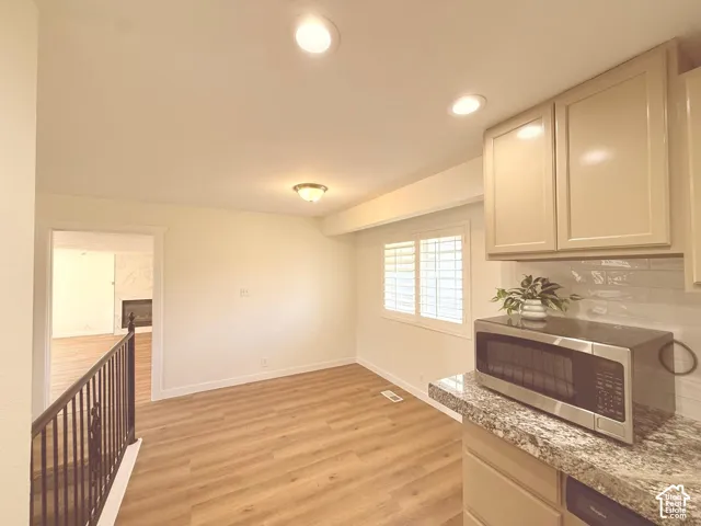 Recessed lighting, wood-finish flooring, white plantation shutters, white subway tile backsplash, and light-toned cabinetry