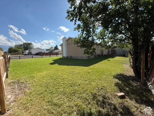 Expansive grassy yard with perimeter fencing, a mature tree, and a stucco exterior on the structure