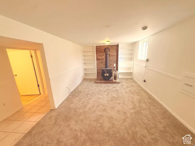 Brick accent wall with a wood-burning stove, built-in shelving, plush carpet flooring, and a tiled entry