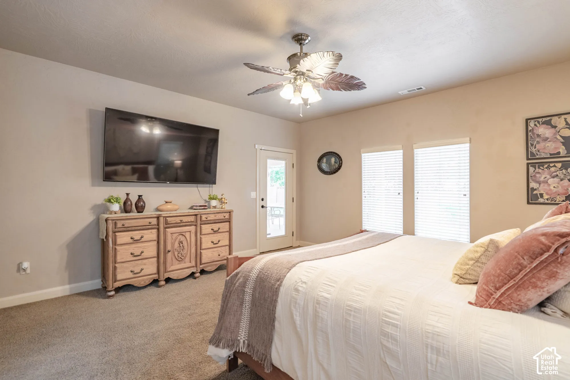 Recessed ceiling, ceiling fan with light fixture, carpeted flooring, wall-mounted television, and exterior door with frosted glass