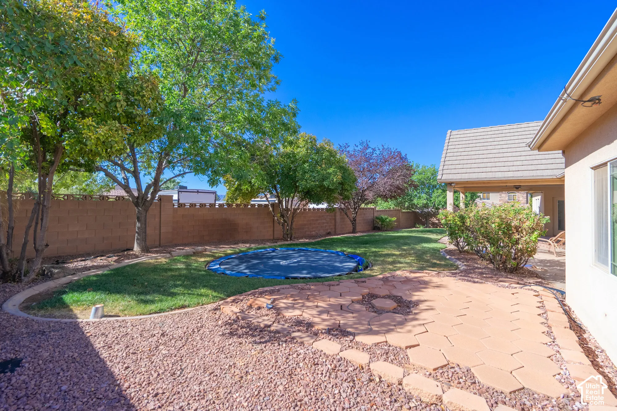 Expansive backyard featuring a manicured lawn, established trees, and a stone paver patio