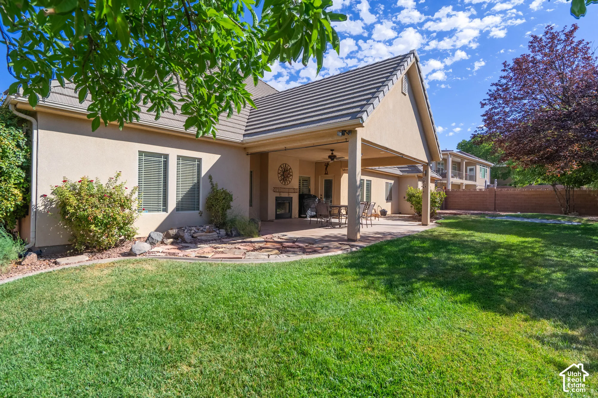 Expansive backyard featuring a manicured lawn, covered patio, outdoor fireplace, and mature landscaping