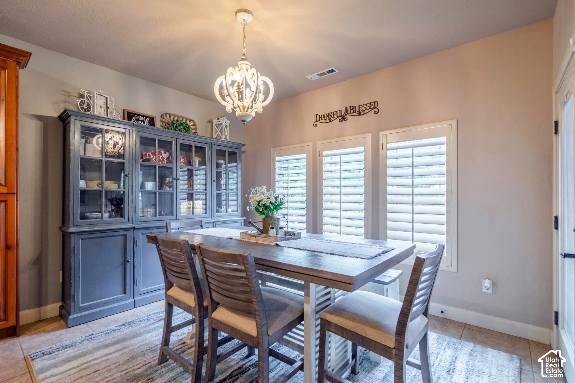 Recessed lighting, three windows with plantation shutters, tile flooring, and a decorative chandelier