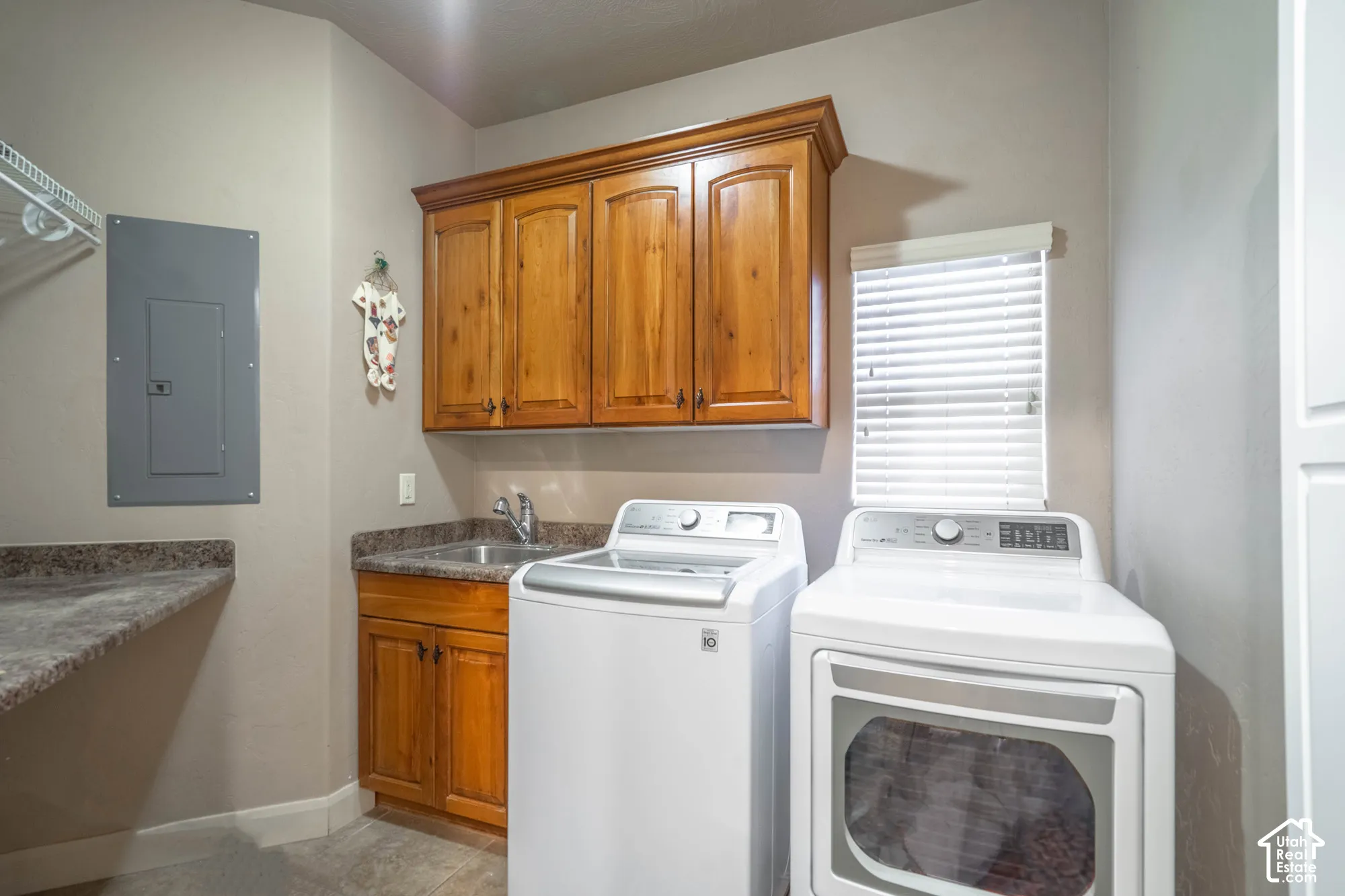 Laundry area with wood-finish cabinetry, stainless steel sink, and light-toned countertops
