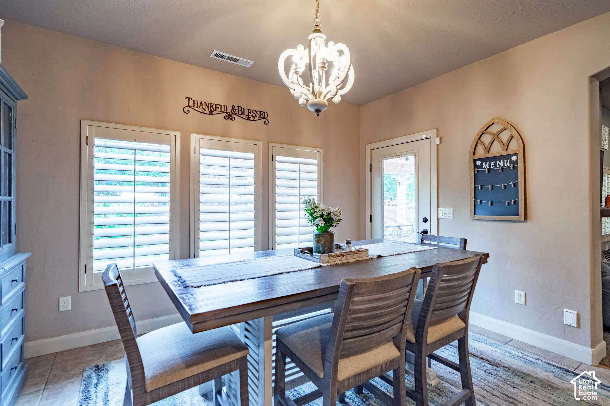 Dining area featuring a decorative chandelier, multiple windows with plantation shutters, and tiled flooring
