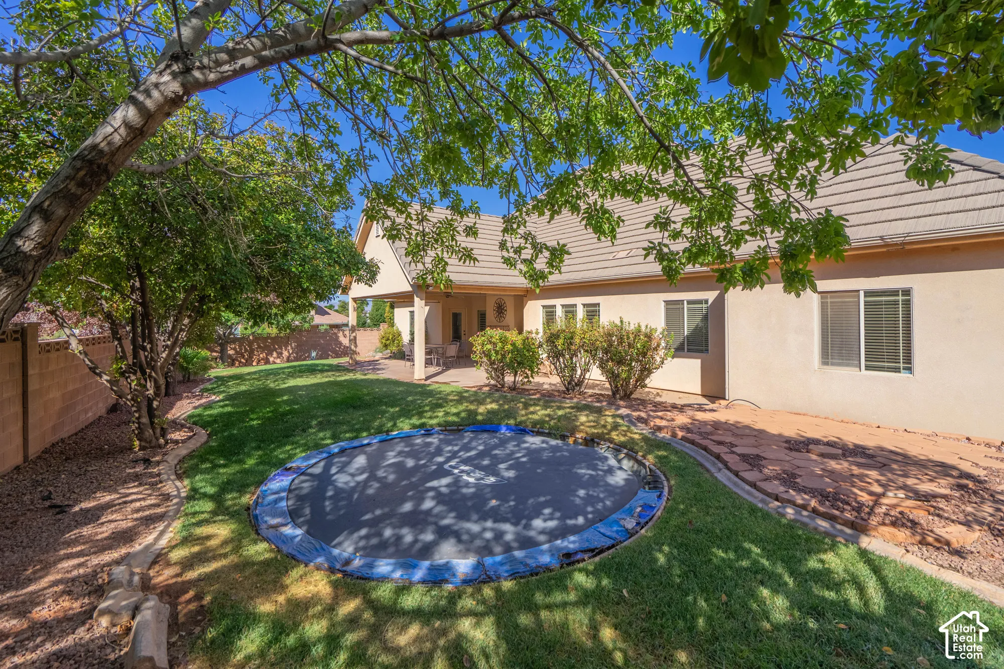 Expansive backyard featuring a manicured lawn, established trees, and a covered patio
