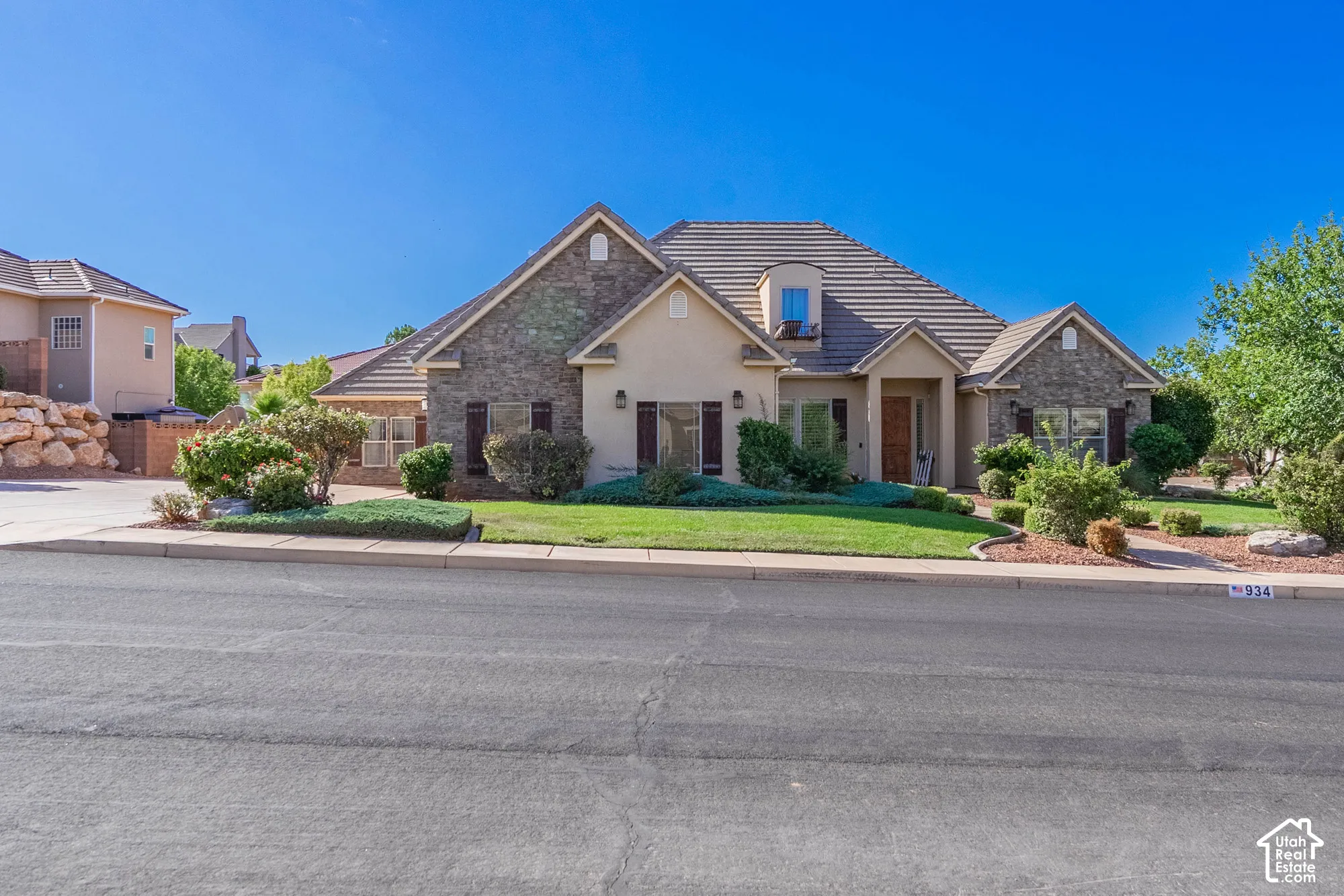 Stucco and stone exterior with a tile roof, featuring a dormer window and mature landscaping