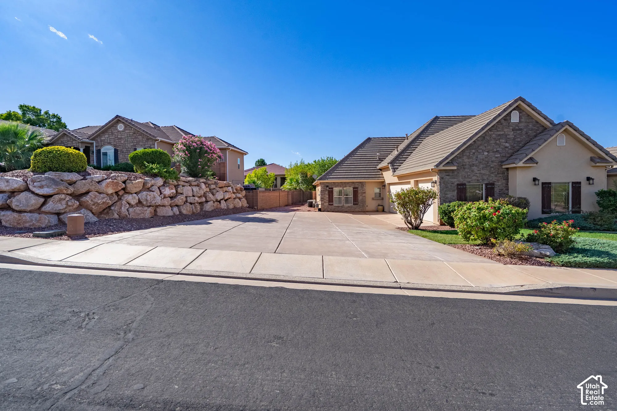 Stucco and stone exterior, multi-car driveway, tile roofing, mature landscaping, and an integrated garage