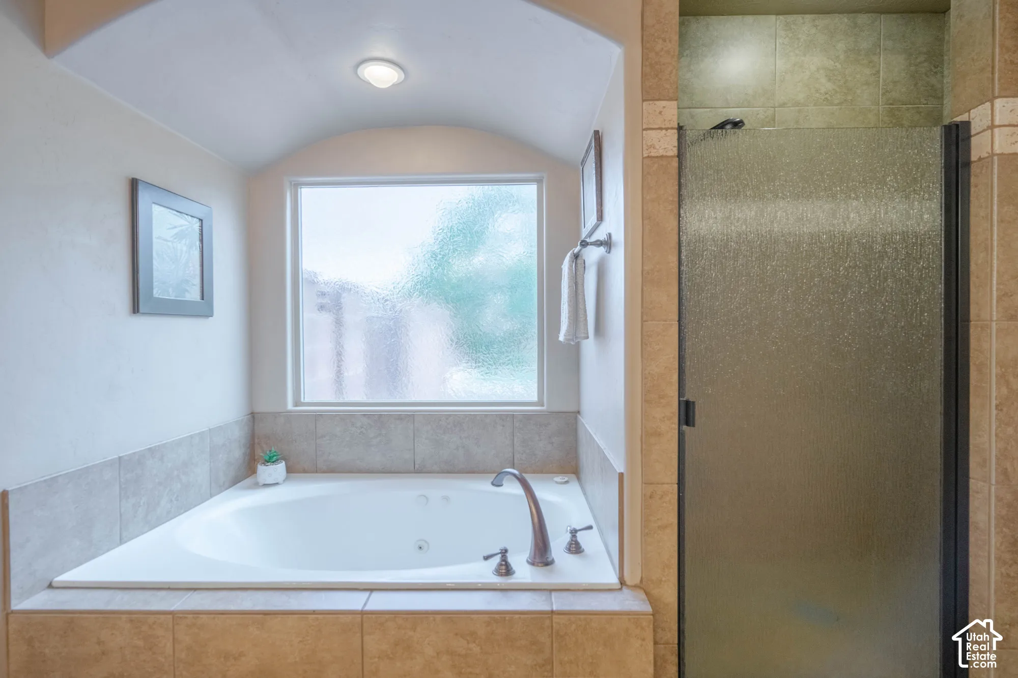 Jetted soaking tub with bronze-finish fixtures, tile surround, and an arched ceiling detail
