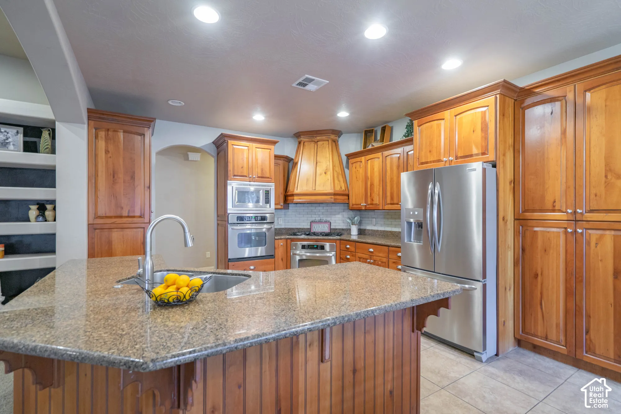 Kitchen with wood cabinetry, stainless steel appliances, a center island with a sink, and recessed lighting