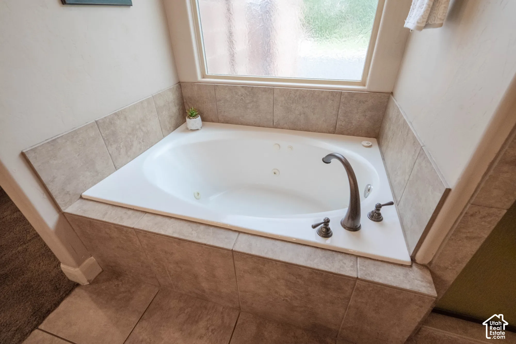 Jetted soaking tub with bronze-finish fixtures, set within a tiled surround and featuring a privacy window