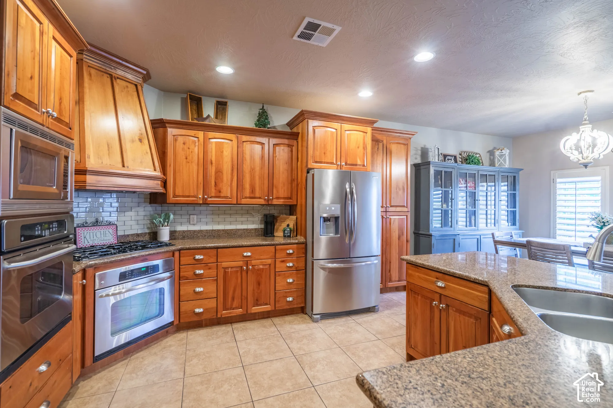 Wood-finish cabinetry, stainless steel appliances, tile flooring, stone countertops, and recessed lighting