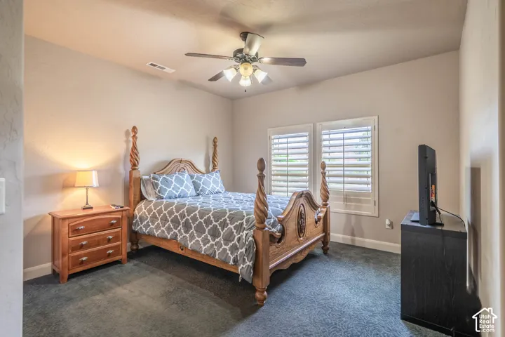Carpeted flooring, vaulted ceiling, ceiling fan with integrated lighting, two windows with plantation shutters, and light-toned wall paint