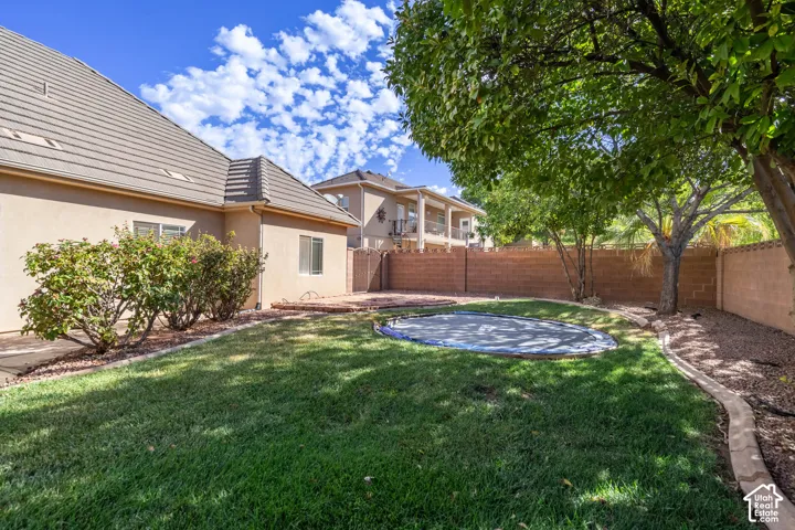 Expansive backyard featuring a manicured lawn, established landscaping, and a privacy wall