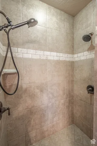 Tiled shower stall featuring a dual shower head system, integrated handheld shower, decorative accent tile band, and a built-in corner shelf