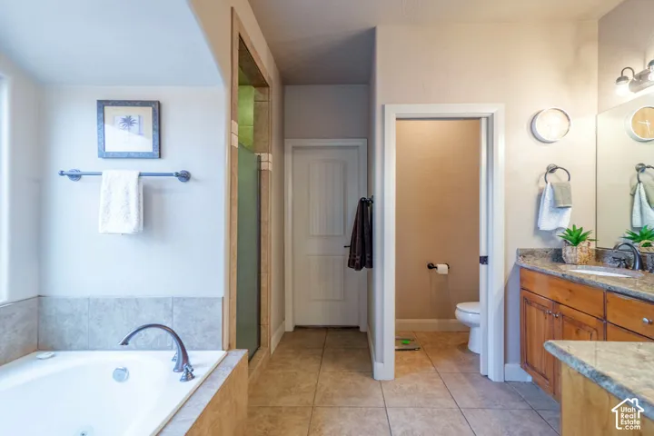 Built-in jetted tub with tile surround, glass-enclosed shower, dual vanity with stone countertop, wood-finish cabinetry, and tiled flooring