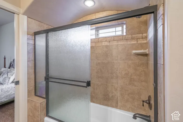 Bathtub with textured glass sliding doors, bronze-finish fixtures, and tile surround with decorative brick-patterned accent