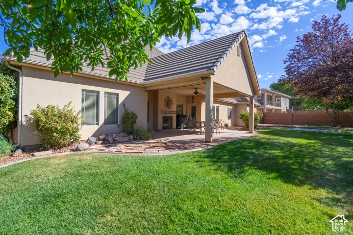 Expansive backyard featuring a manicured lawn, covered patio, outdoor fireplace, and mature landscaping