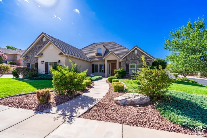 Stucco exterior with stone accents, a tiled roof, a curved walkway, and landscaped grounds featuring mature plantings and green lawn